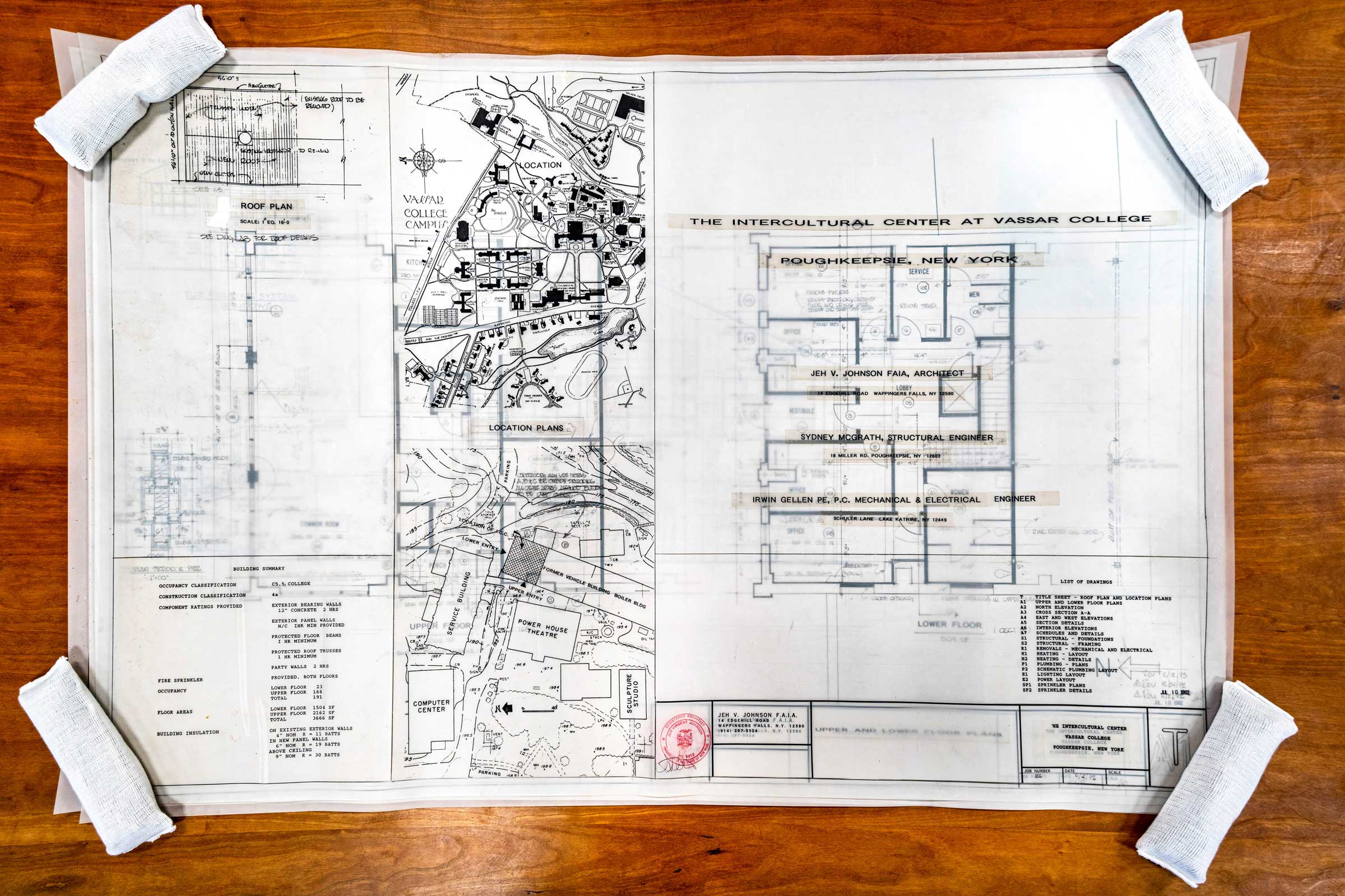 Overhead view of architectural plans on paper on a desk held down by weights in the corners.