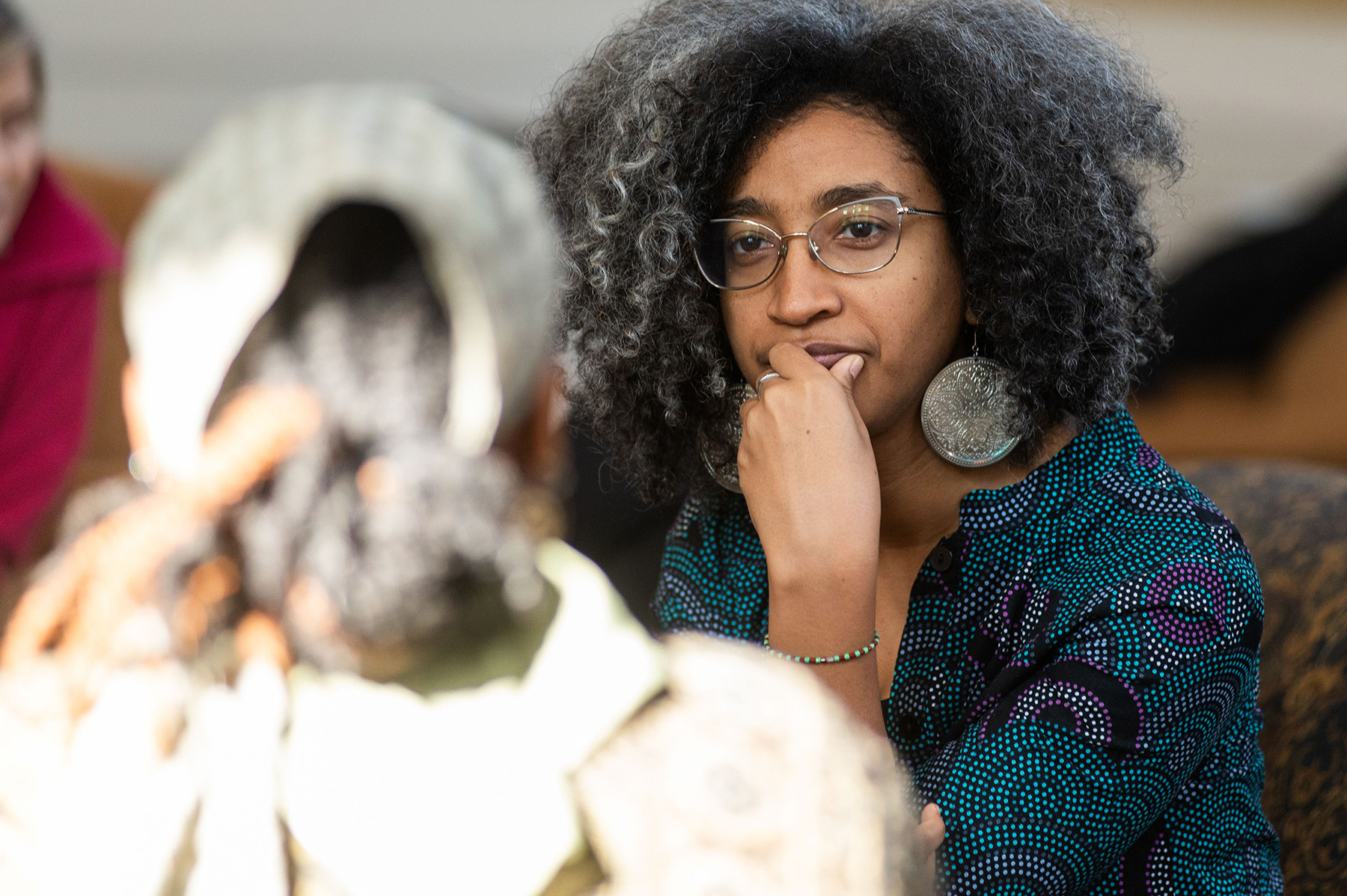 Person sitting with their hand to their mouth looking at a person across from them at a table. Overlayed is the "Black History Month" logo.