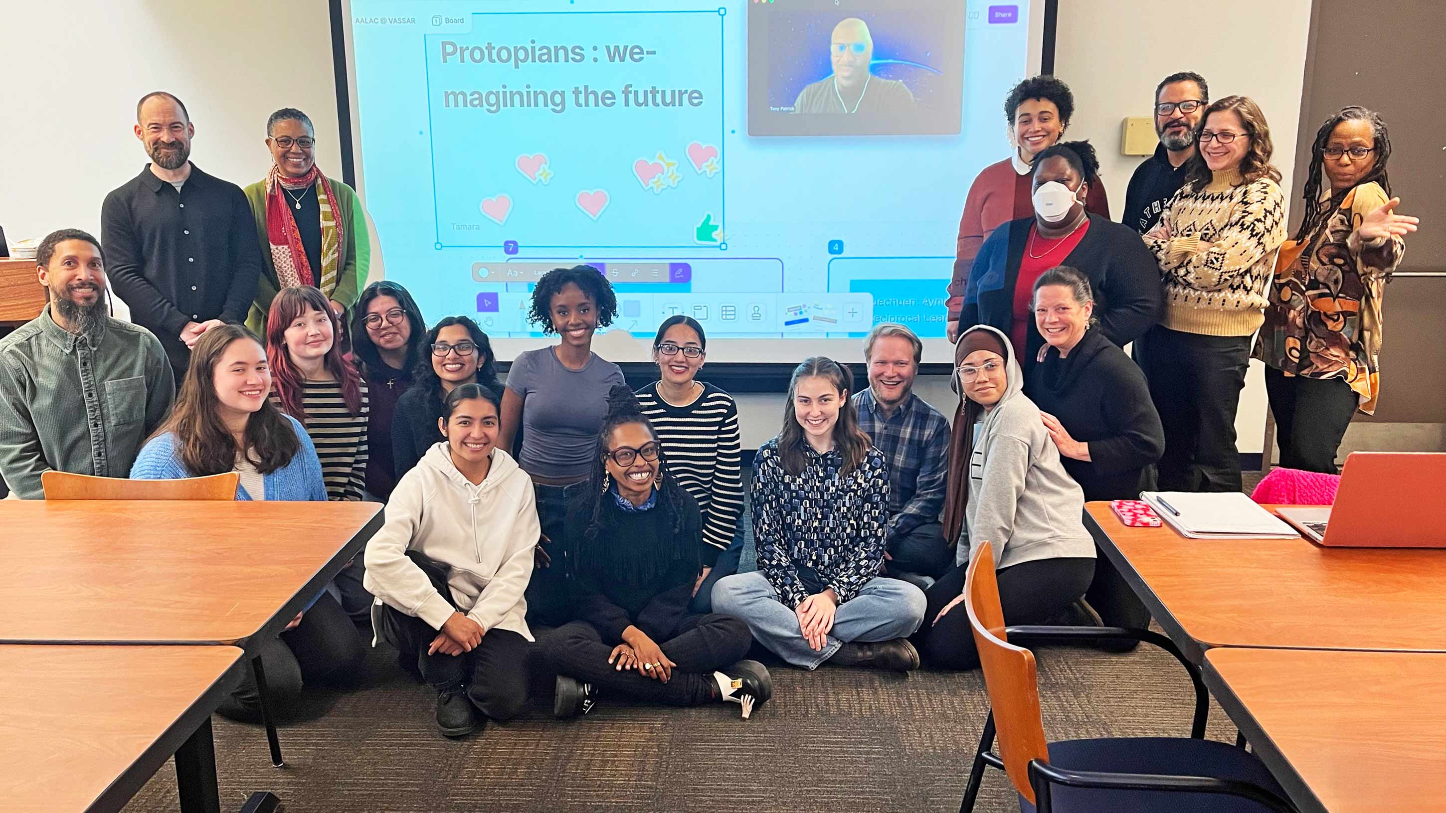 A group of people in a classroom posing in front of a screen with a presentation slide reading 'Protopians: we-imagining the future'.