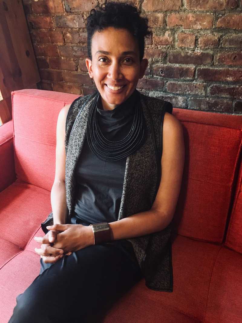 A person with short black hair sits on a red chair smiling at the camera.