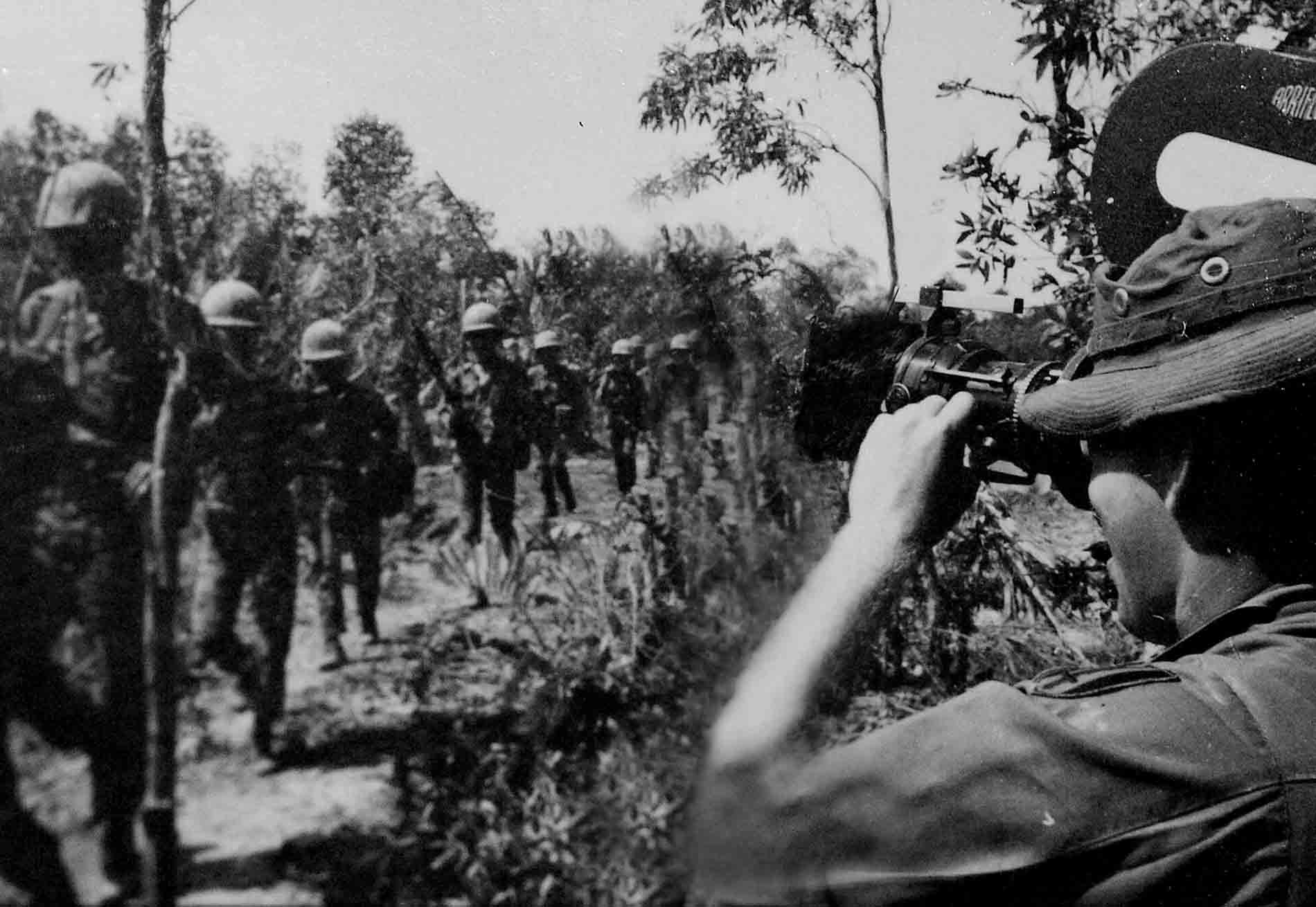 Cinematographer filming soldiers as they march by in a line.