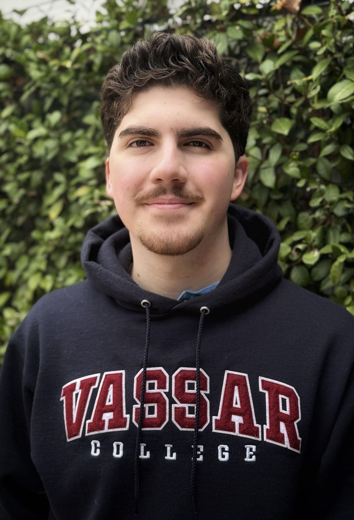 Person standing outside in front of a bush wearing a Vassar College sweatshirt.
