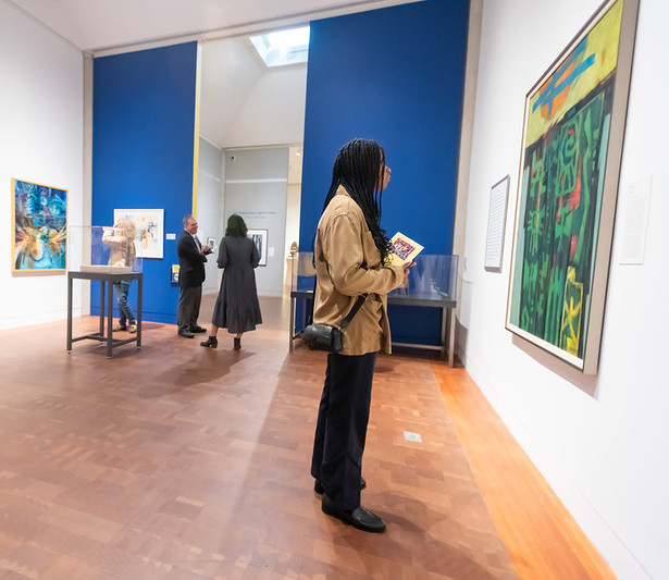 A person stands in a large art gallery, looking at a work on the wall.