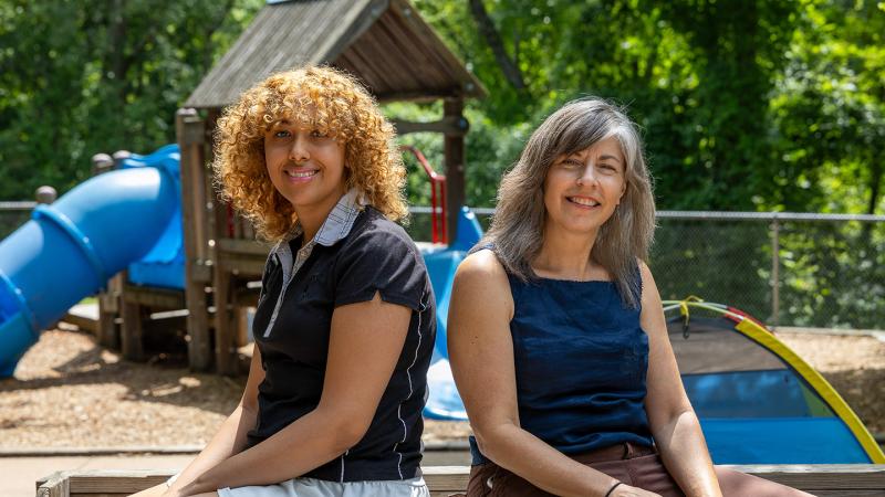 Student and professor seated facing the camera with a playground in the background.