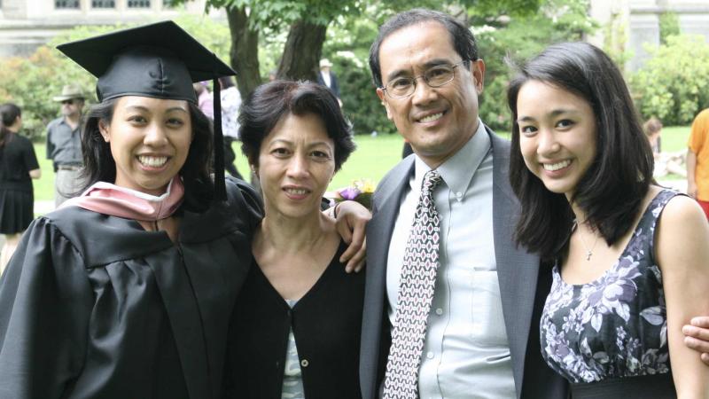 Four people smiling at the camera. One of the people is dressed in graduation robes.