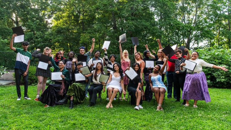 A large group of students who are standing in two lines holding up a diploma and smiling. 