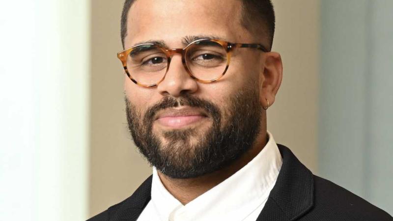 A portrait of Stephen Andrade, a person with short black hair and beard, glasses, and a dark suit coat.