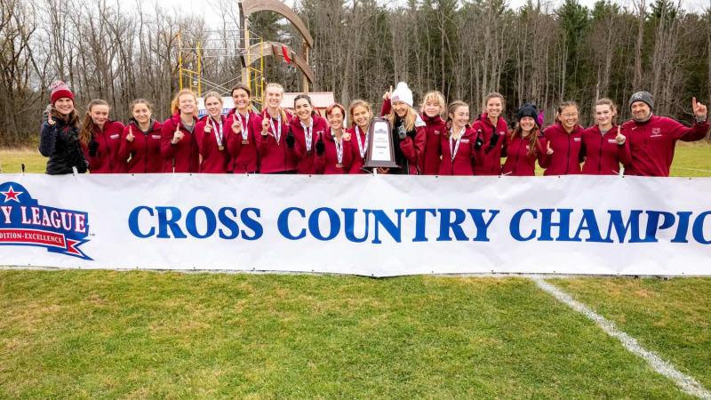 Large group of smiling athletes standing behind a banner that reads: cross country champions.