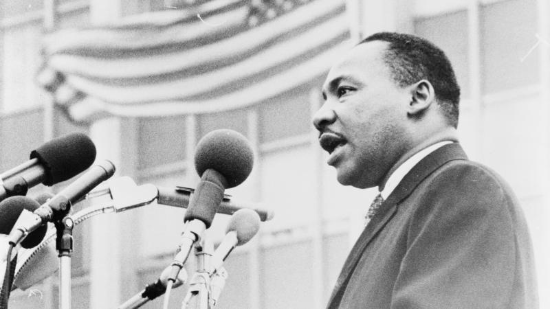 Martin Luther King Jr. speaking in front of a row of microphones.