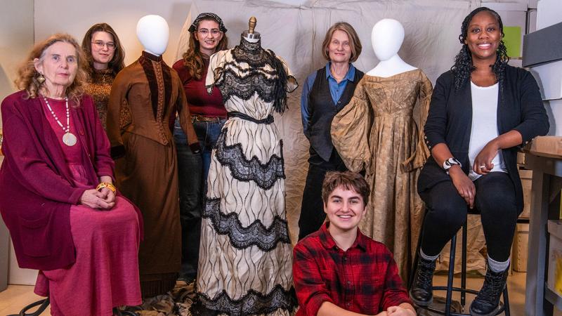 A group standing among a few mannequins adorned with dresses.