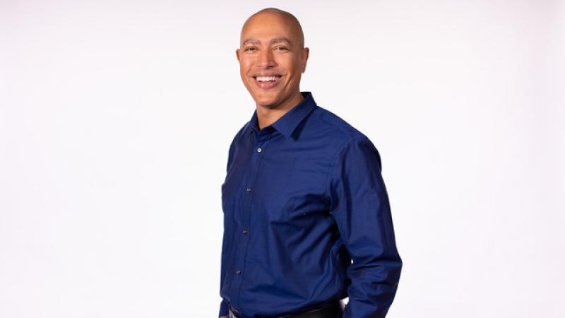 Portrait photo of Torrey Maldonado standing and smiling with his hands in his pockets.