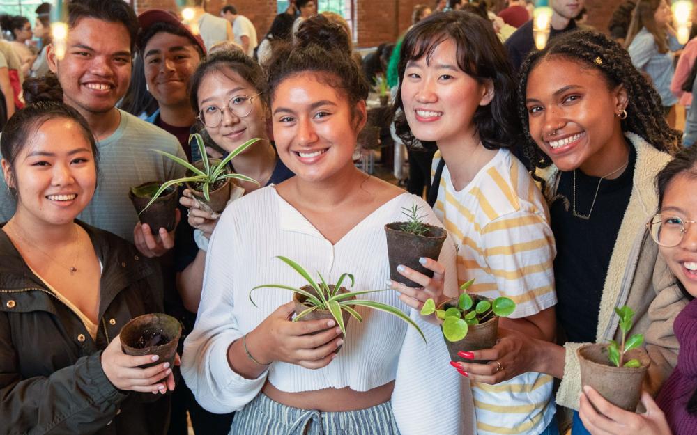 A large group of people standing and holding small potted plants.