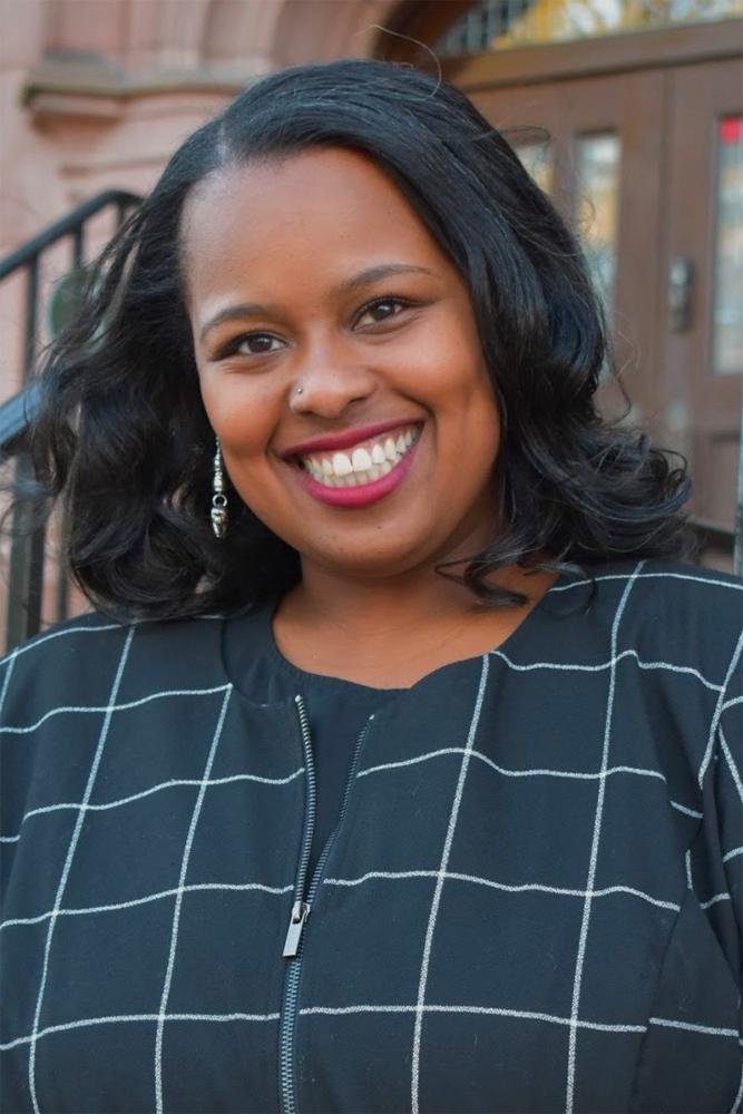 Pictured: Taneisha N. Means. Portrait of a person standing in front of a building.