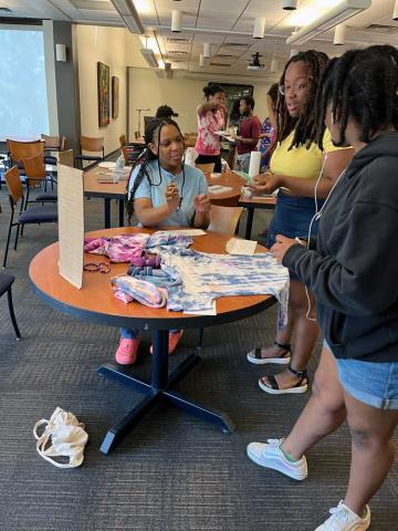 Three people seated around a table working on a tie-die t-shirt