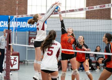 Several people on opposite sides of a volleyball net jumping to hit/block the ball while jumping with their hands up.