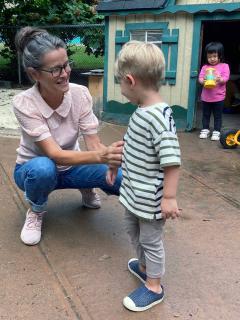 Carol Murray squatting down to speak to a toddler while another toddler looks on