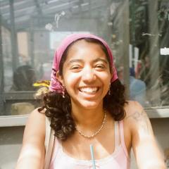 Person smiling wearing a pink bandana and pink tank top.