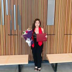 Angela Kim wearing black pants and a black top holding a bouquet of flowers and diploma.