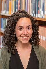 Person with long curly brown hair standing in front of a book case.