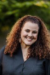 A portrait of Carolyn Kulic, a person with long brown curly hair and a gray shirt.