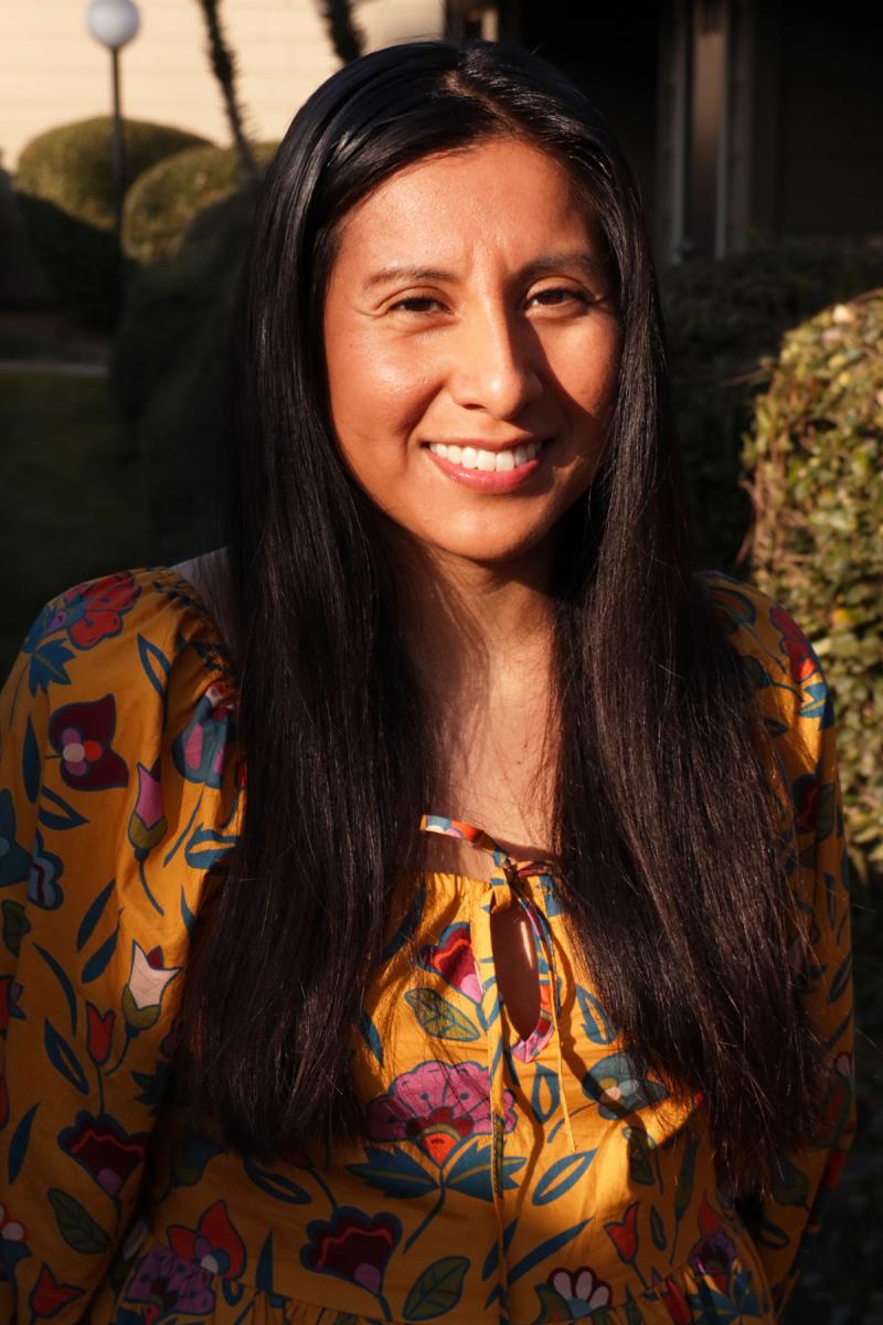 Candy Martinez headshot wearing an orange flower patterned shirt and has long dark hair.