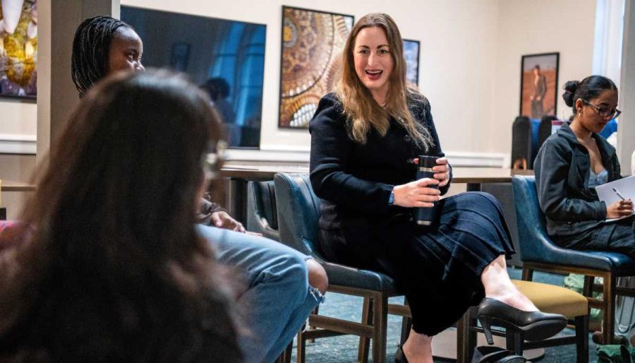 Dr. Michelle Monje ’98, a person with long blond hair and a dark dress, sits in a room talking to some other people.