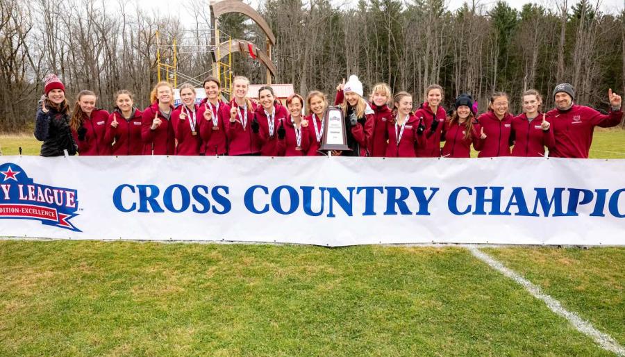 Large group of smiling athletes standing behind a banner that reads: cross country champions.