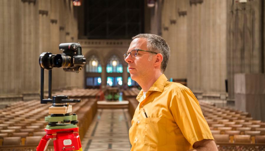 Andrew Tallon wearing a yellow shirt inside the Washington National Cathedral with a camera on a tripod. 