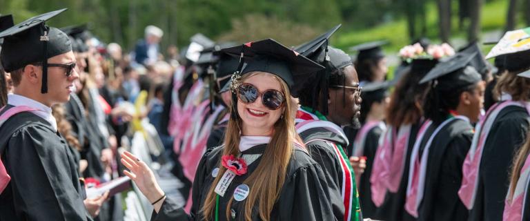 Person in graduation ceremony attire standing in a crowd of other graduates smiling for the camera.