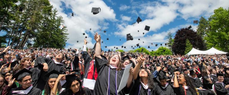 Joyful graduation ceremony hat toss outside with blue skies and fluffy clouds.