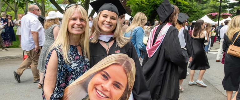 One person in graduation ceremony attire smiling and giving a side hug to another person.