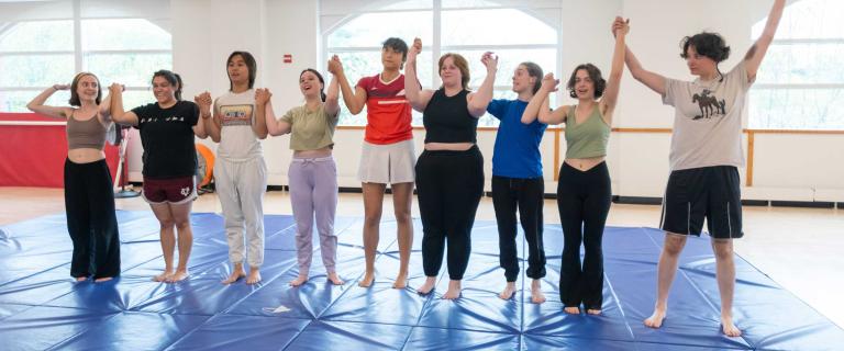 A group of people in a line holding each other's hands up and smiling while standing on a gym mat.