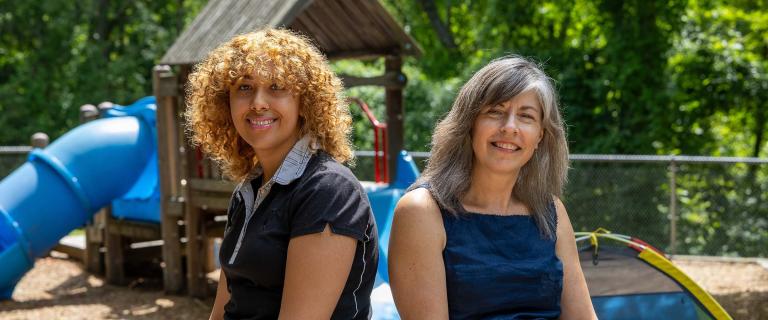 Student and professor seated facing the camera with a playground in the background.