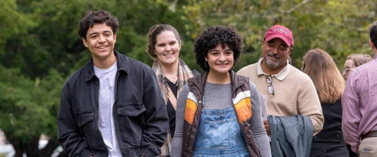 A group of smiling people walking outdoors and taking in fall foliage.