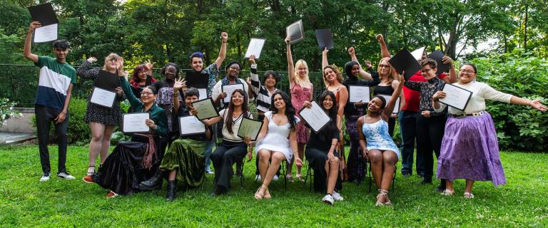 A large group of students who are standing in two lines holding up a diploma and smiling. 