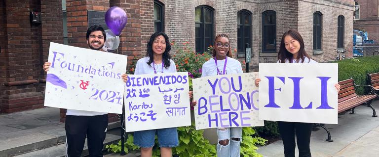 A group of four students with welcome signs greeting new students.