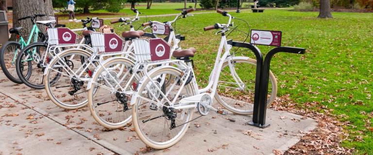 Uniform white bicycles parked in a bicycle program bike rack.