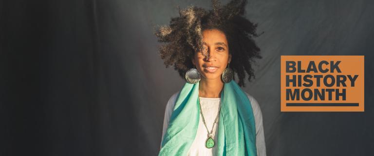 Alexis Pauline Gumb poses in front of a grey background, with a 'Black History Month' badge overlaid.