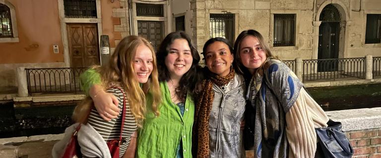 Picture of four people standing outside in a city with their arms around each other smiling.