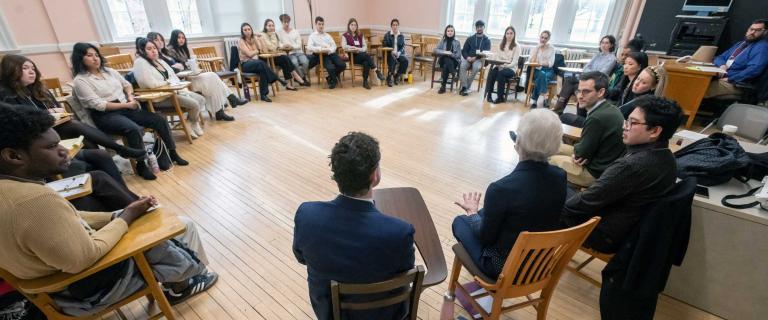 A large group of people seated in a circle listening and speaking.