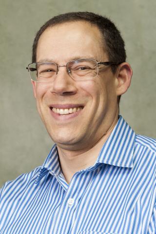 Jeffrey S. Seidman wearing a blue and white striped collared shirt against a light background.
