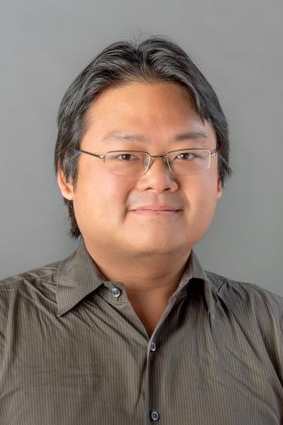 Benjamin Ho wearing a dark tan shirt against a light gray background.