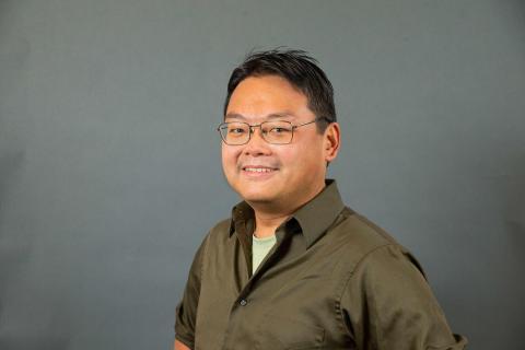 Benjamin Ho wearing a dark tan shirt against a dark gray background.