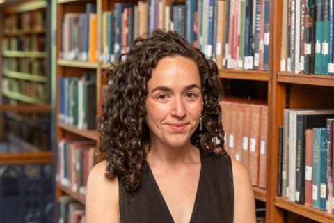 Person with long curly brown hair standing in front of a book case.