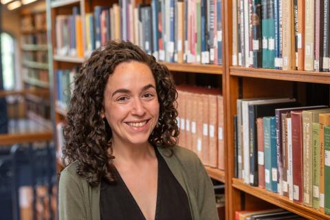 Person with long curly brown hair standing in front of a book case.