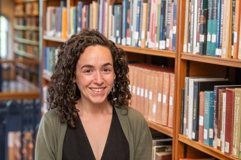 Person with long curly brown hair standing in front of a book case.