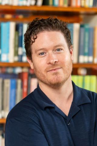 A portrait photo of Mark Taylor posing in front of a bookshelf.