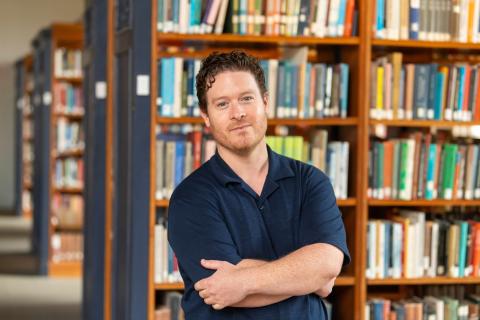 A portrait photo of Mark Taylor posing in front of a bookshelf.