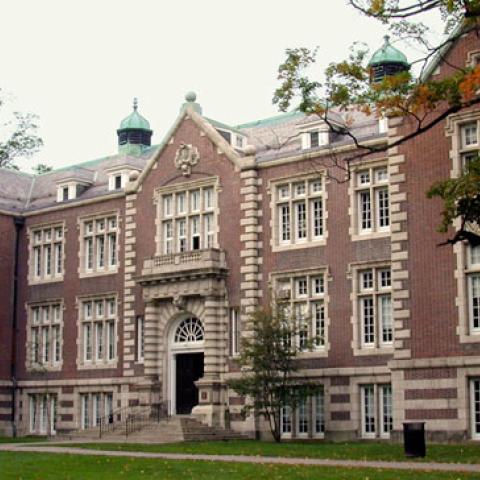 Exterior photo of Rockefeller Hall - a red brick building with tan accent with some trees around the building.bricks and trim, a dark colored roof, and 2 green turrets 