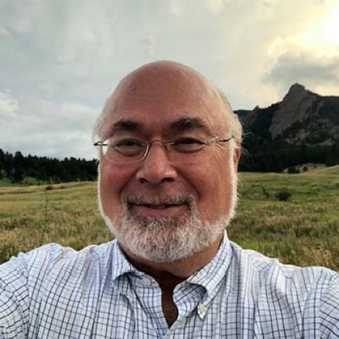 Jonathan Granoff outside with a grassy field and a rocky hill in the background.